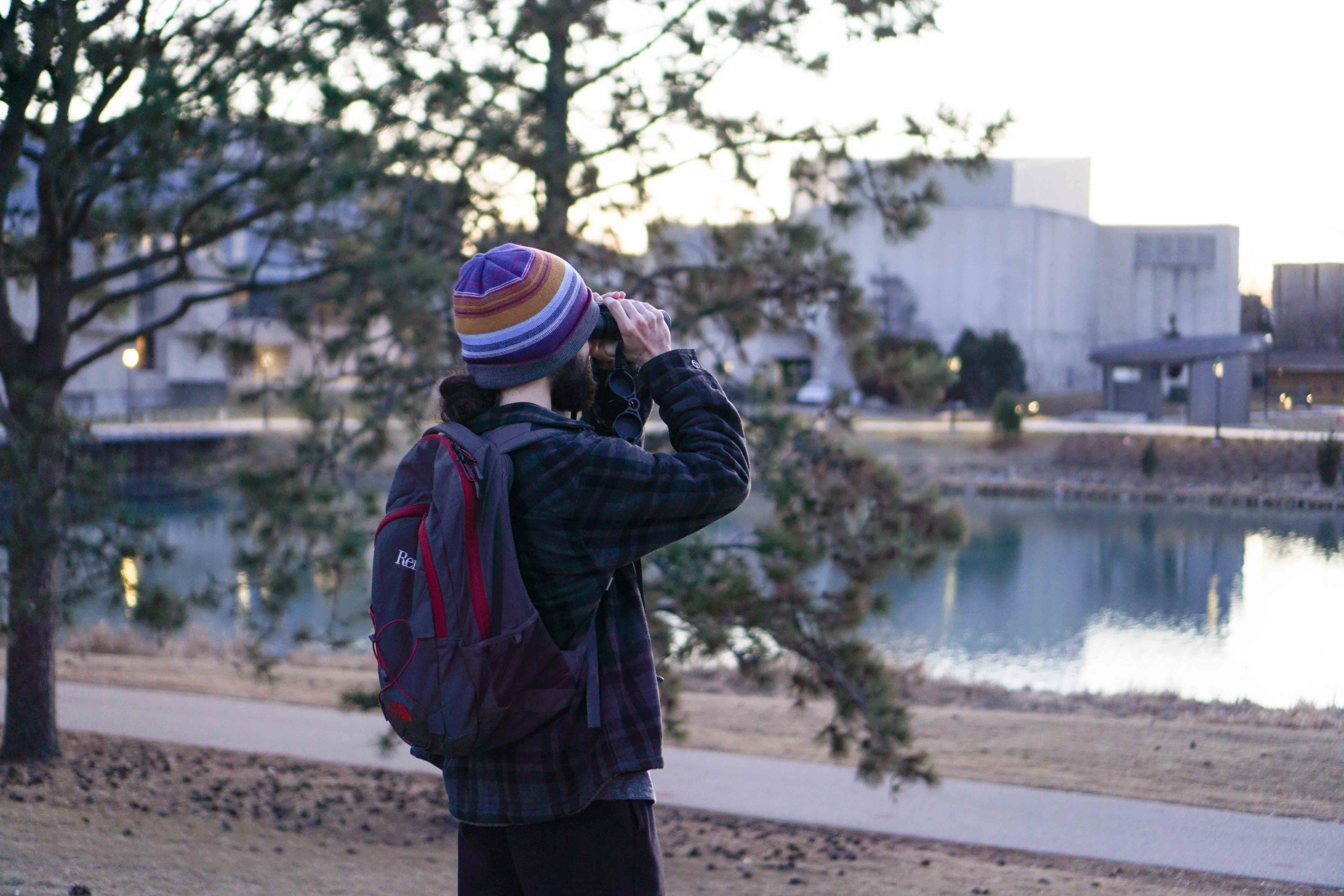 A man with a pair of binoculars looks out across the lake.